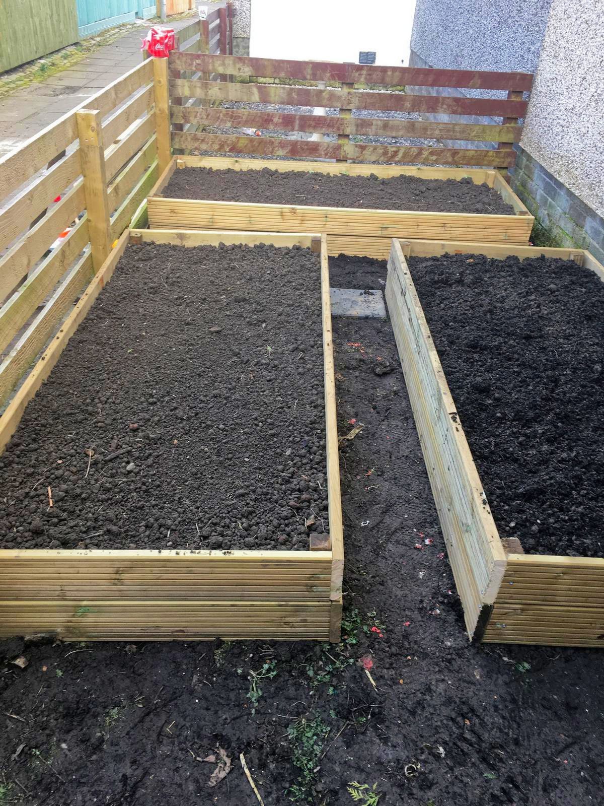 Three wooden planters filled with soil and a wooden fence in the background.