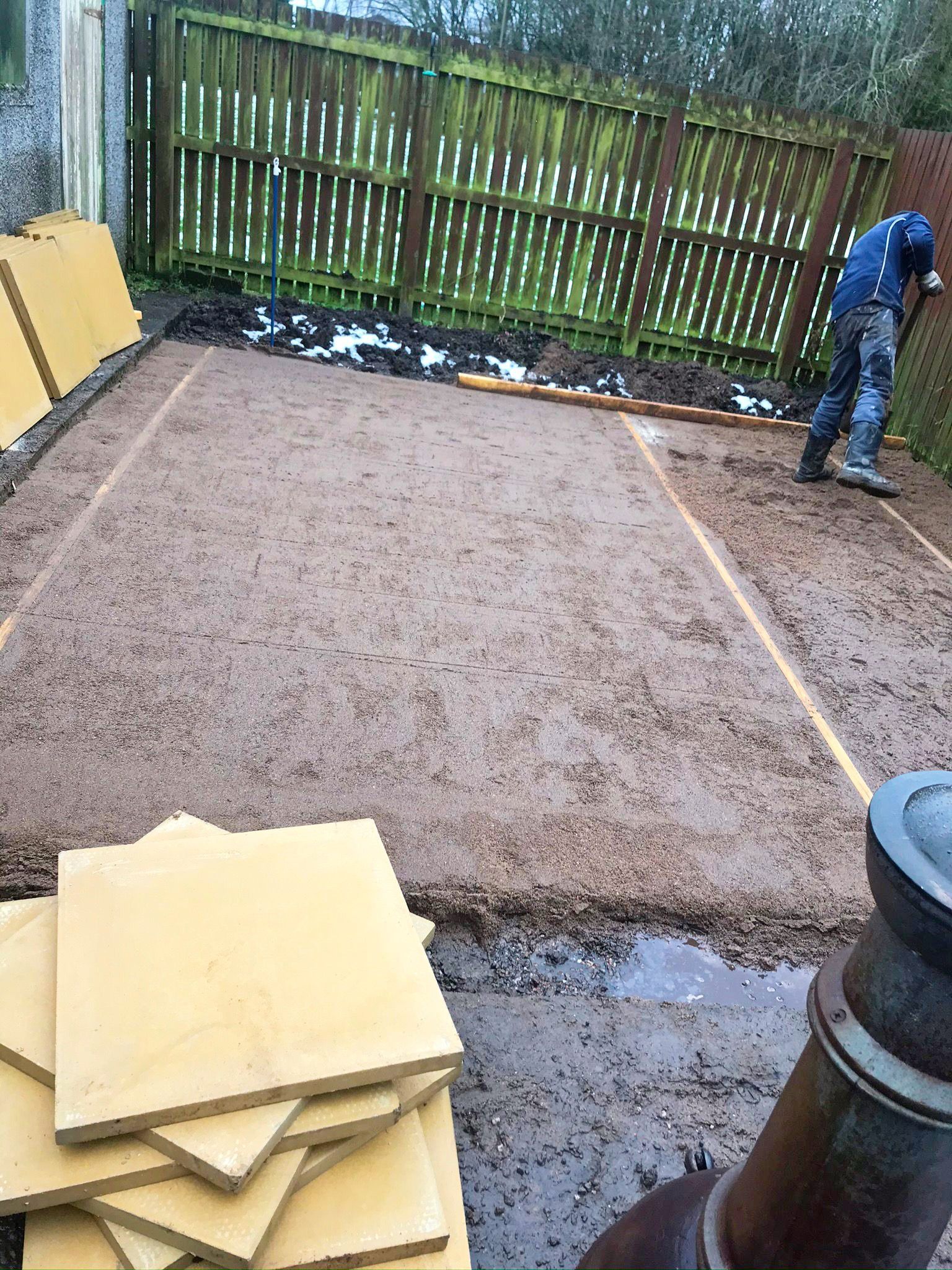 A man is standing on a dirt ground next to a pile of tiles.
