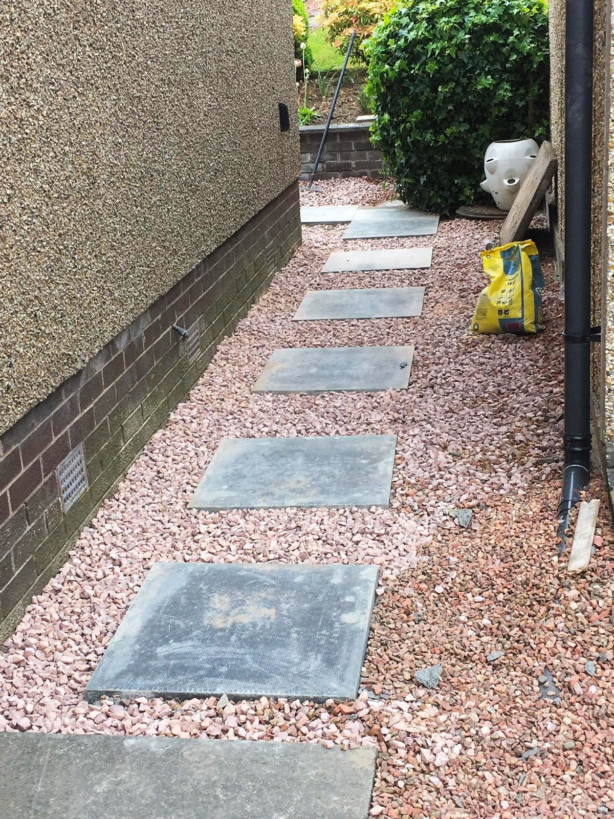 A narrow walkway between two buildings with gravel and stepping stones.