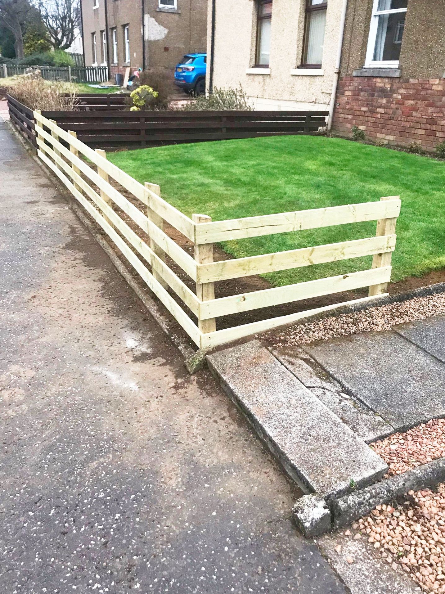 A wooden fence surrounds a lush green lawn in front of a house.