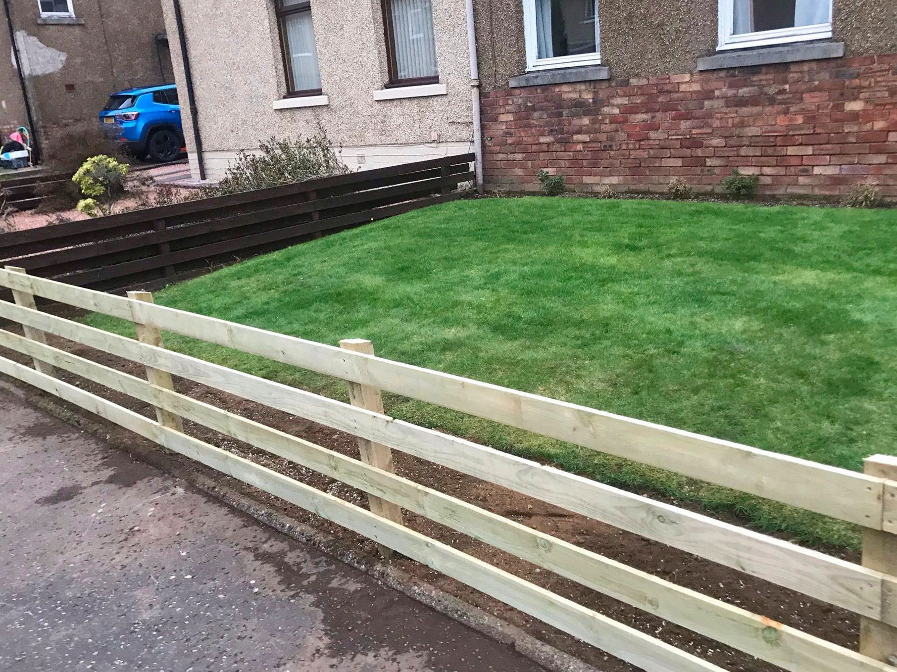 A wooden fence surrounds a lush green lawn in front of a brick building.