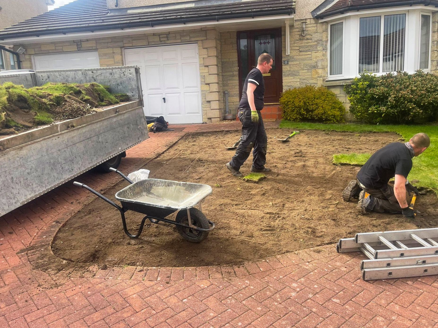 Two men are removing an old front garden lawn.