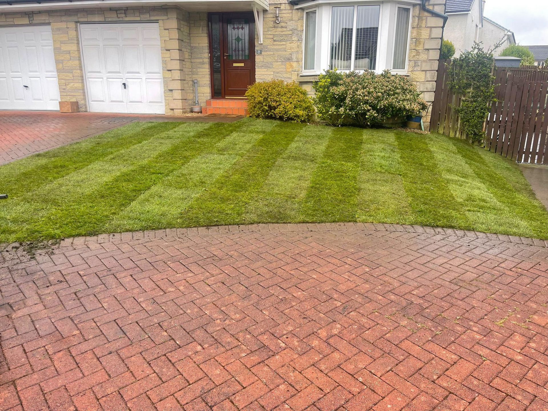 A brick driveway leading to a house with a newly laid lush green lawn.