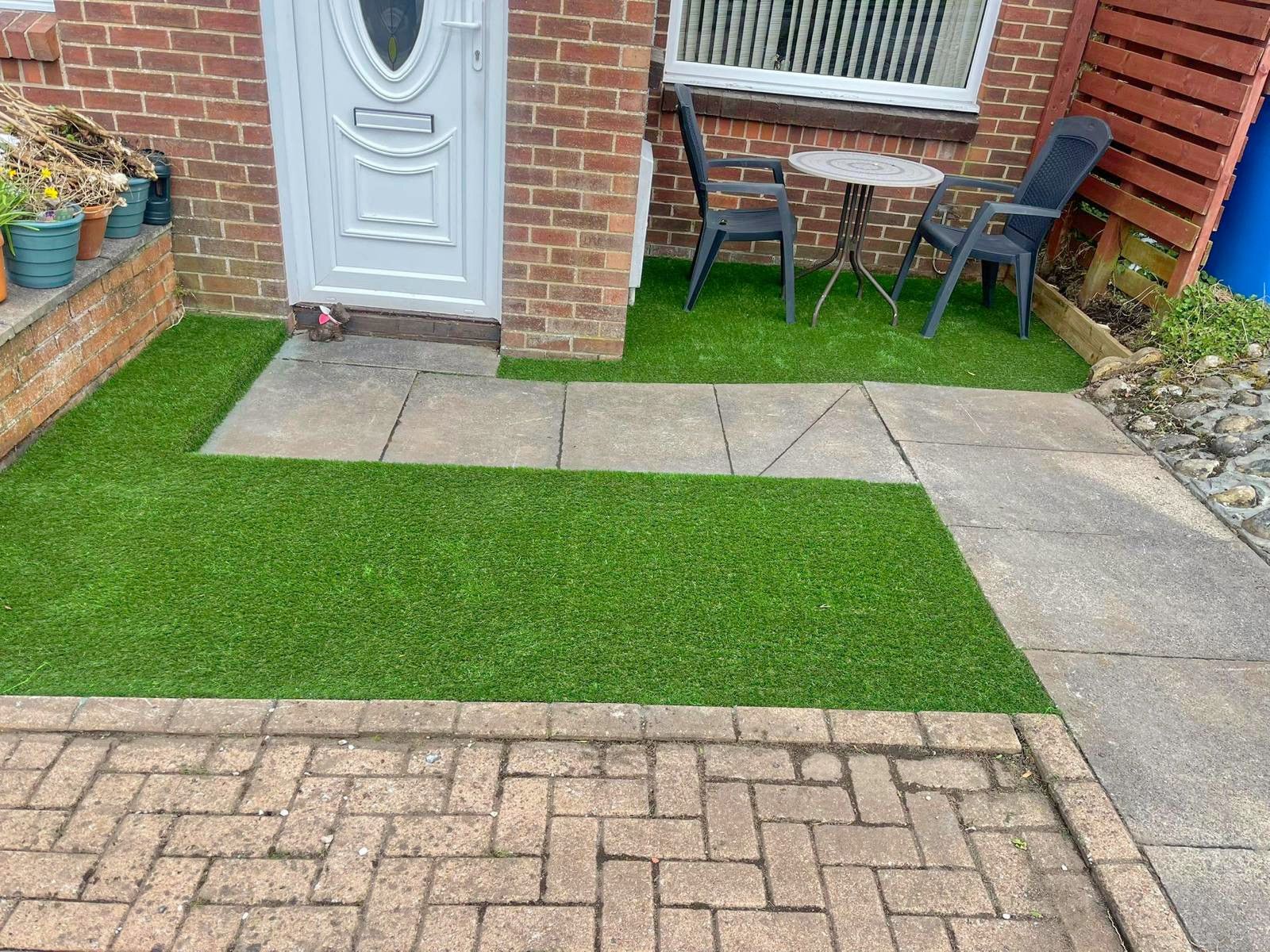 A brick driveway with a table and chairs in front of a brick house. The astro turf completes the project.