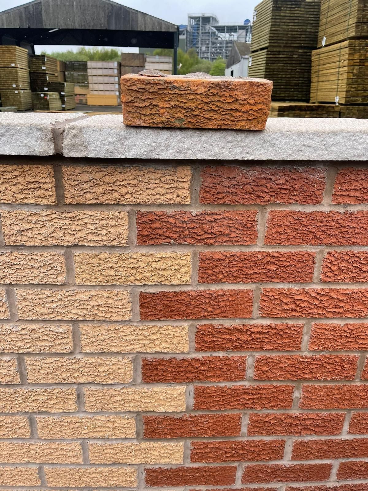 An extended brick wall with a brick sitting on top of it.