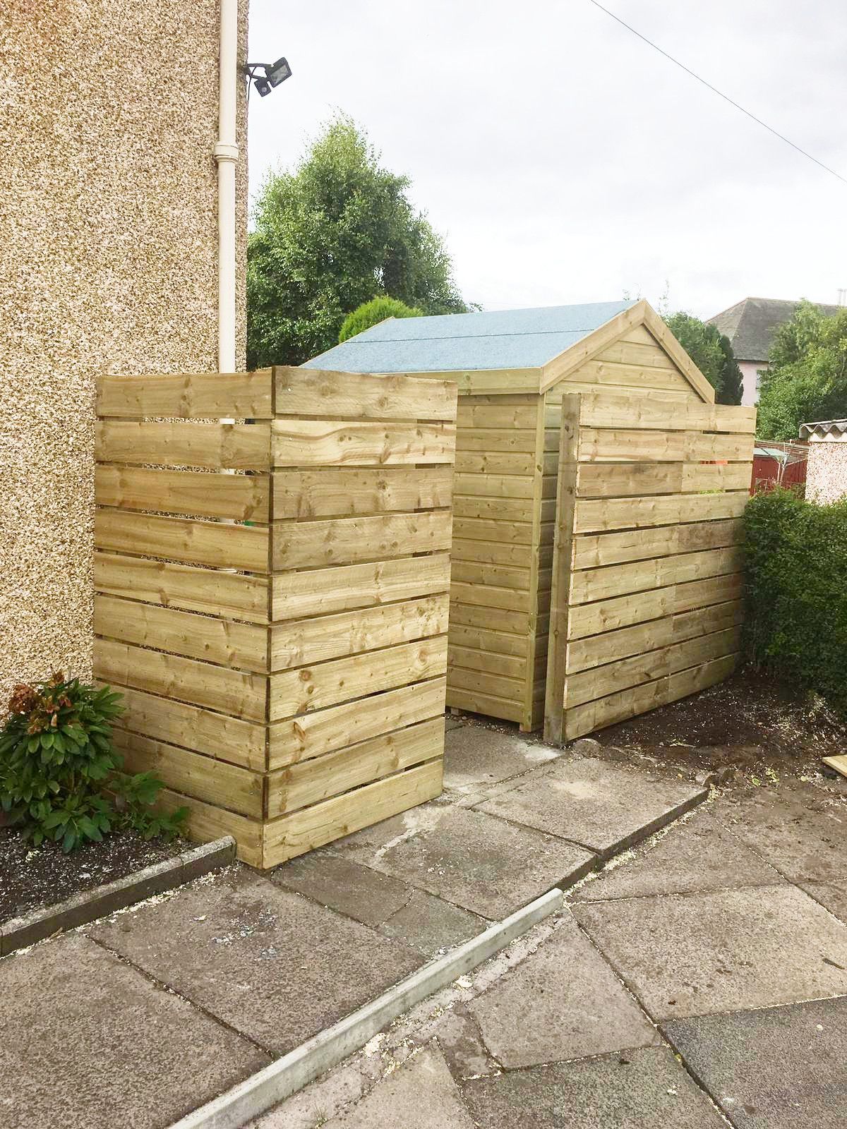 A wooden shed is sitting on the side of a building next to a sidewalk.