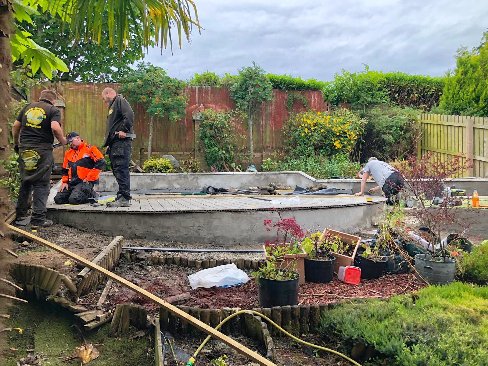 A group of men are working on a round garden patio in a back-garden.