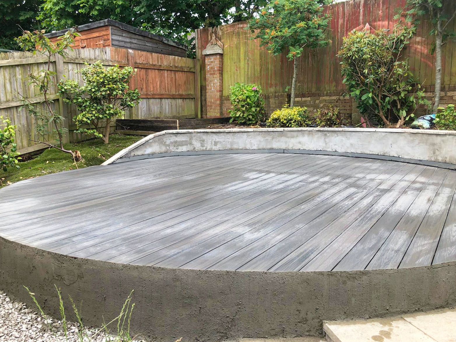 A circular wooden deck is being built in a backyard.