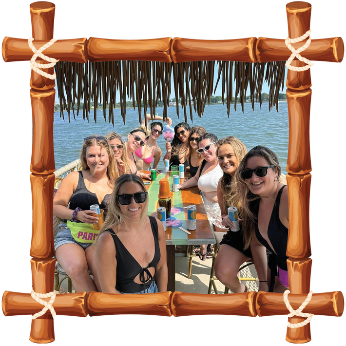 Group of people at a tropical beach table, smiling under a bamboo frame with palm thatch overhead