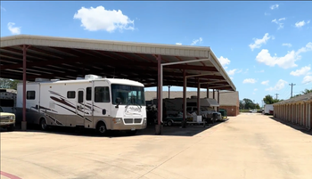 Row of red brick storage units with white garage doors against a clear blue sky.