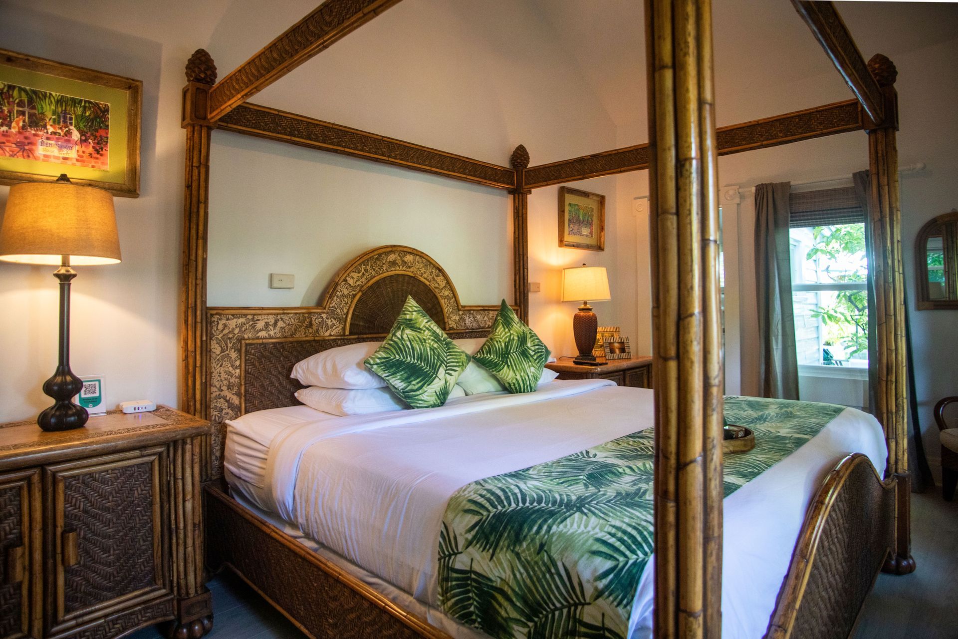 Tropical bedroom with four-poster bed, green leaf bedding, warm lamps, and balcony view