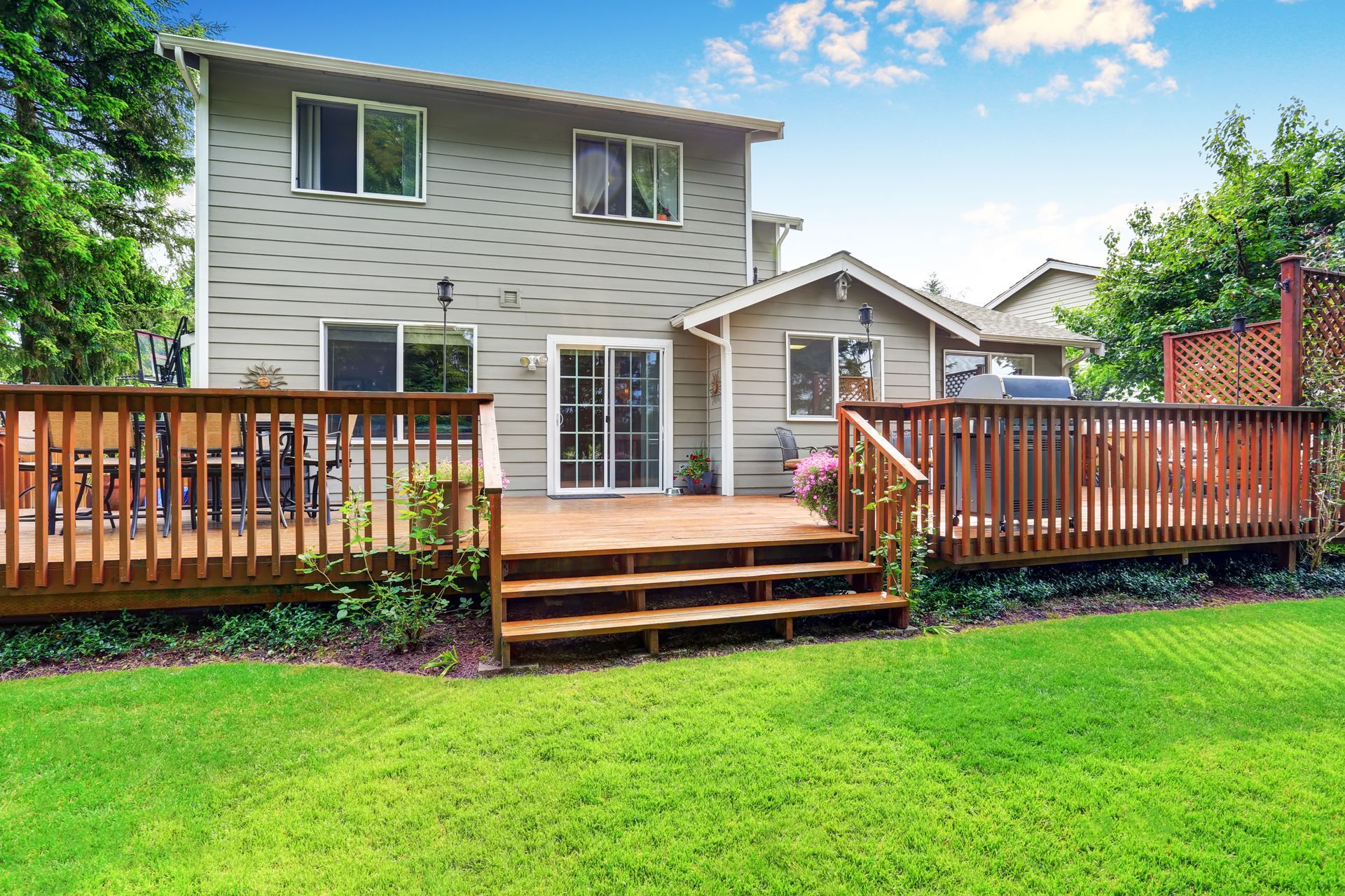 Backyard deck with wooden railings and steps leading to a gray two-story house