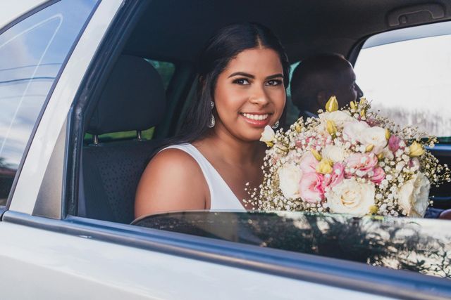 A bride is sitting in the back seat of a car holding a bouquet of flowers.