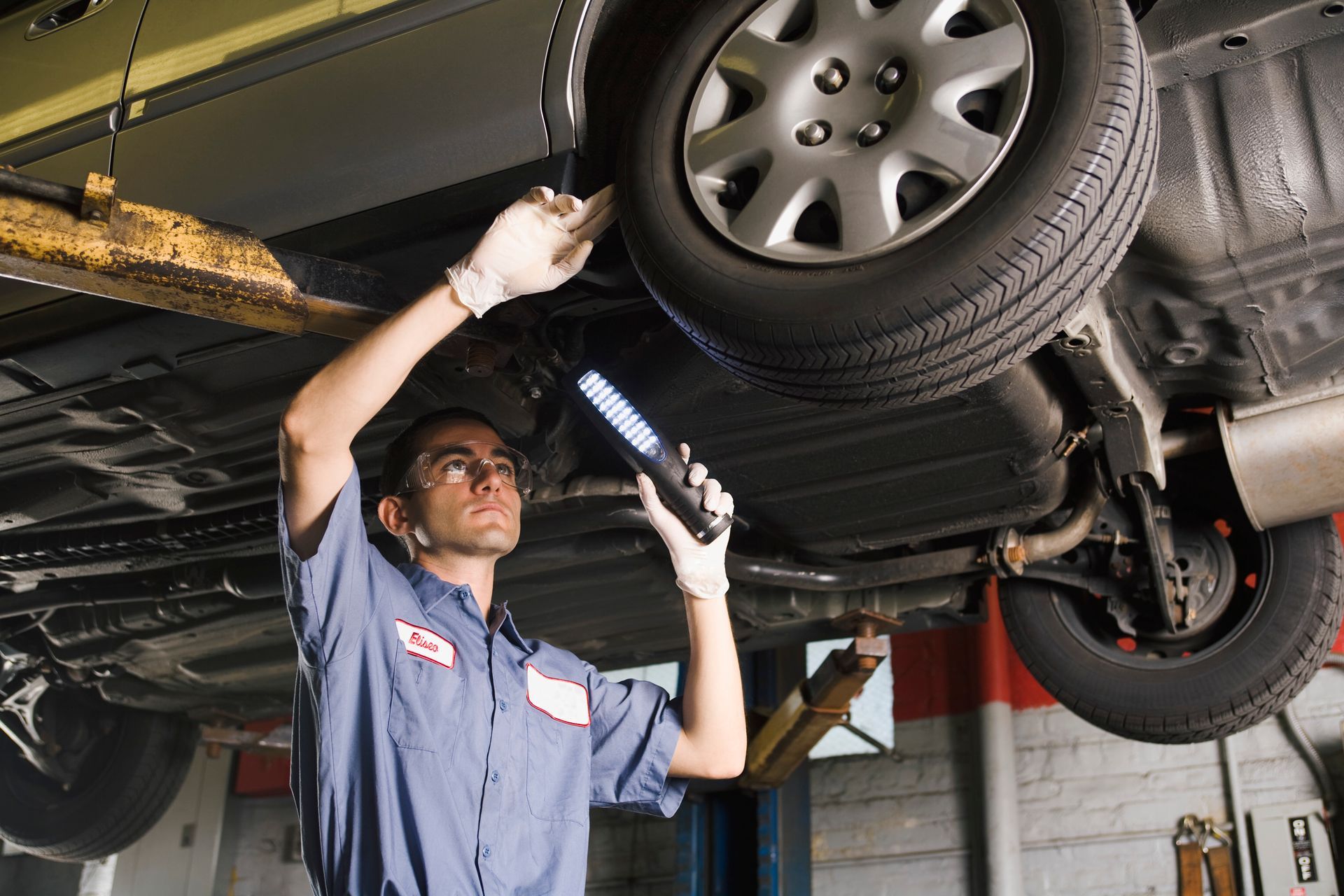 A technician inspects a vehicle with a flashlight at Sam’s Tire Service Inc, specializing in tire repair in Elkhart IN.