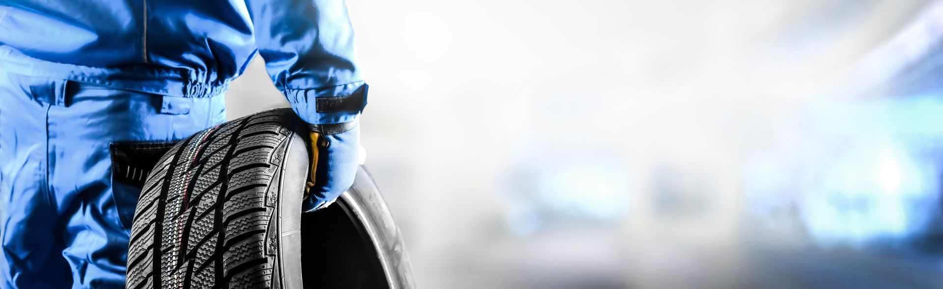 Auto technician in blue coveralls holding a tire in a brightly lit workshop