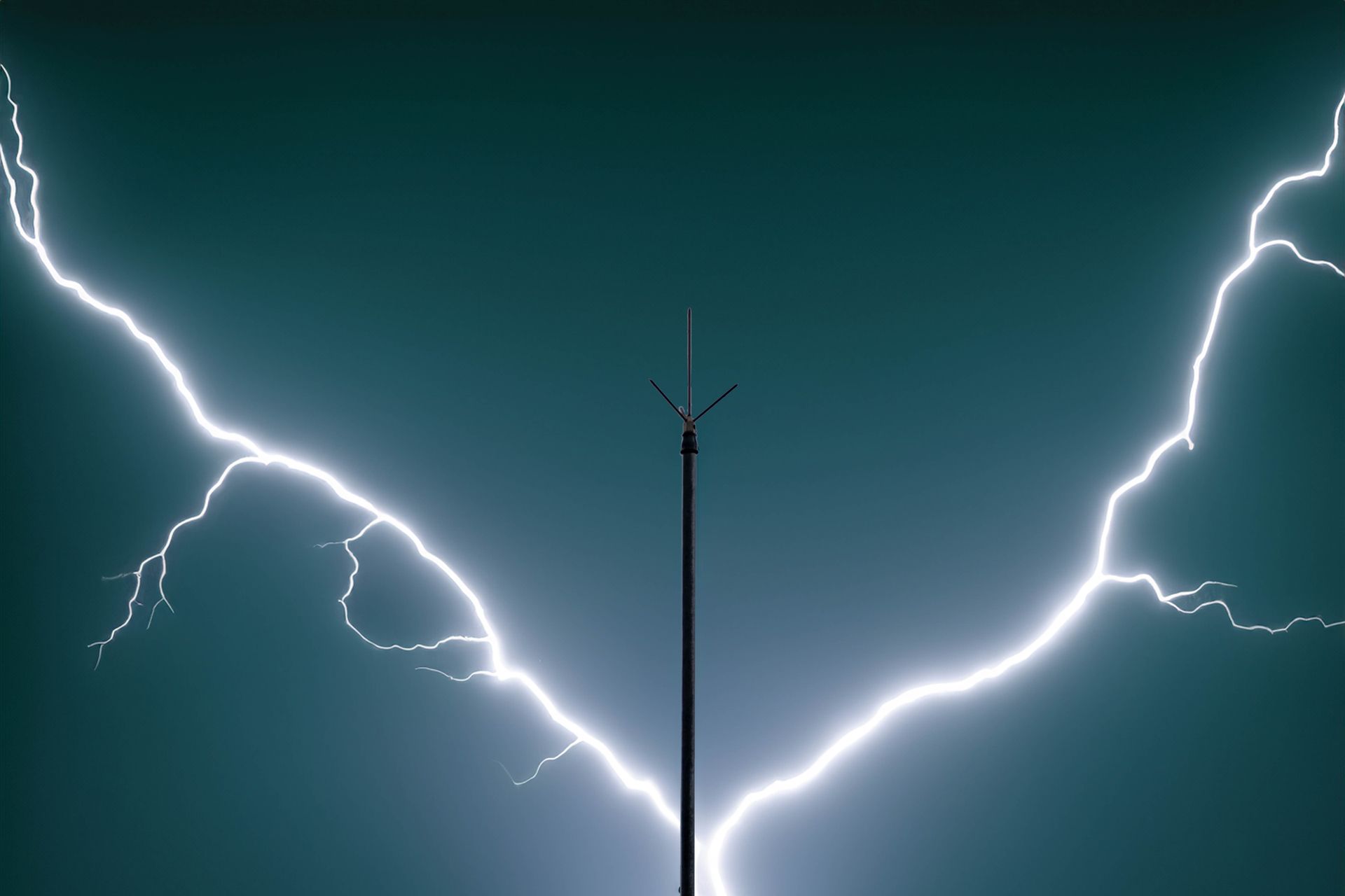 An electrician in work clothes holds stripped wires while repairing a wall-mounted electrical outlet with tools on the floor.