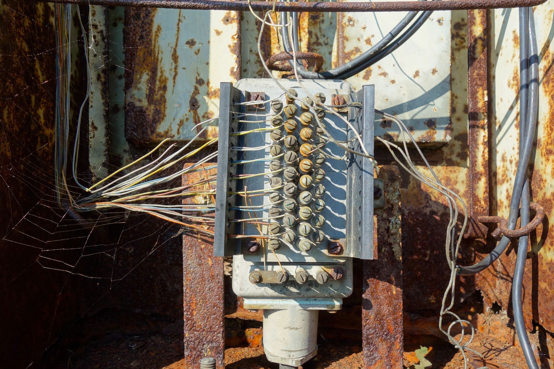 Weathered industrial terminal block with connected wires mounted against a rusted metal wall.