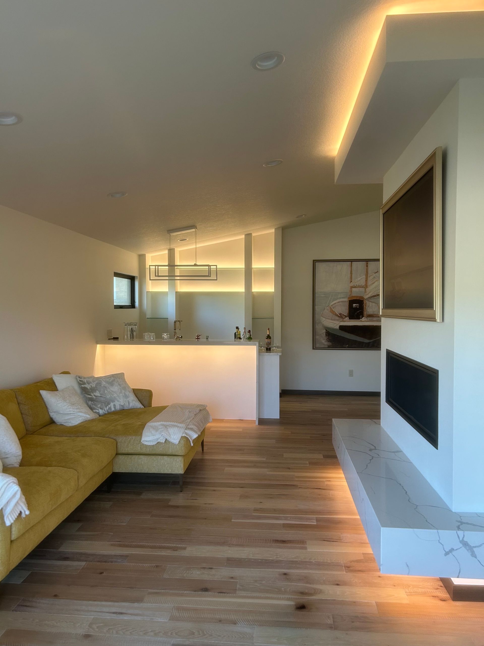 An electrician in a hard hat and gloves stands on a ladder, installing a square LED light fixture into a white ceiling.