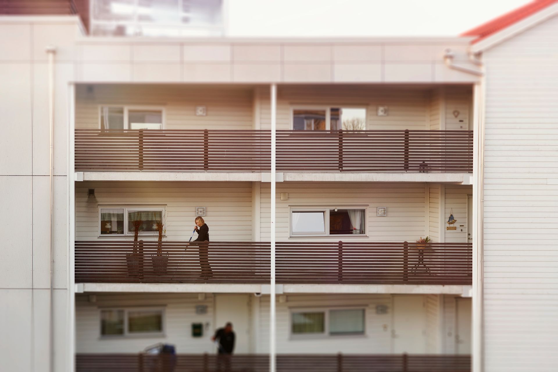 Fleretasjes bygning med balkonger. Folk står på en balkong, to andre er synlige på bakkenivå.