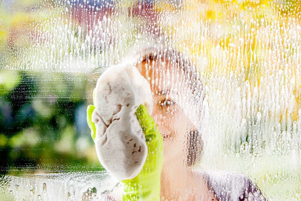 Person wearing green gloves cleaning a window with a sponge, blurred background.