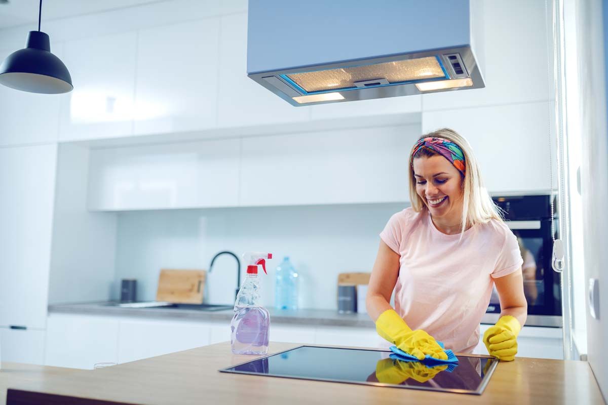 Woman in yellow gloves cleaning kitchen cooktop.
