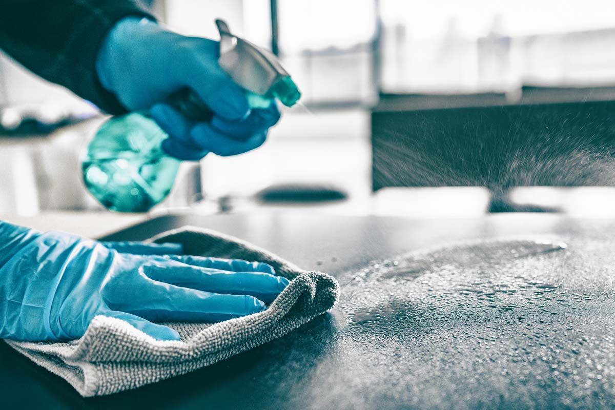 Hender i blå hansker sprayer og tørker av en mørk overflate med en klut.