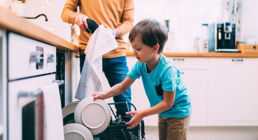 A person and a child loading a dishwasher in a kitchen.