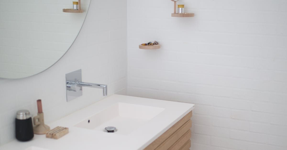 White bathroom with a sink, a round mirror, and wooden shelves.
