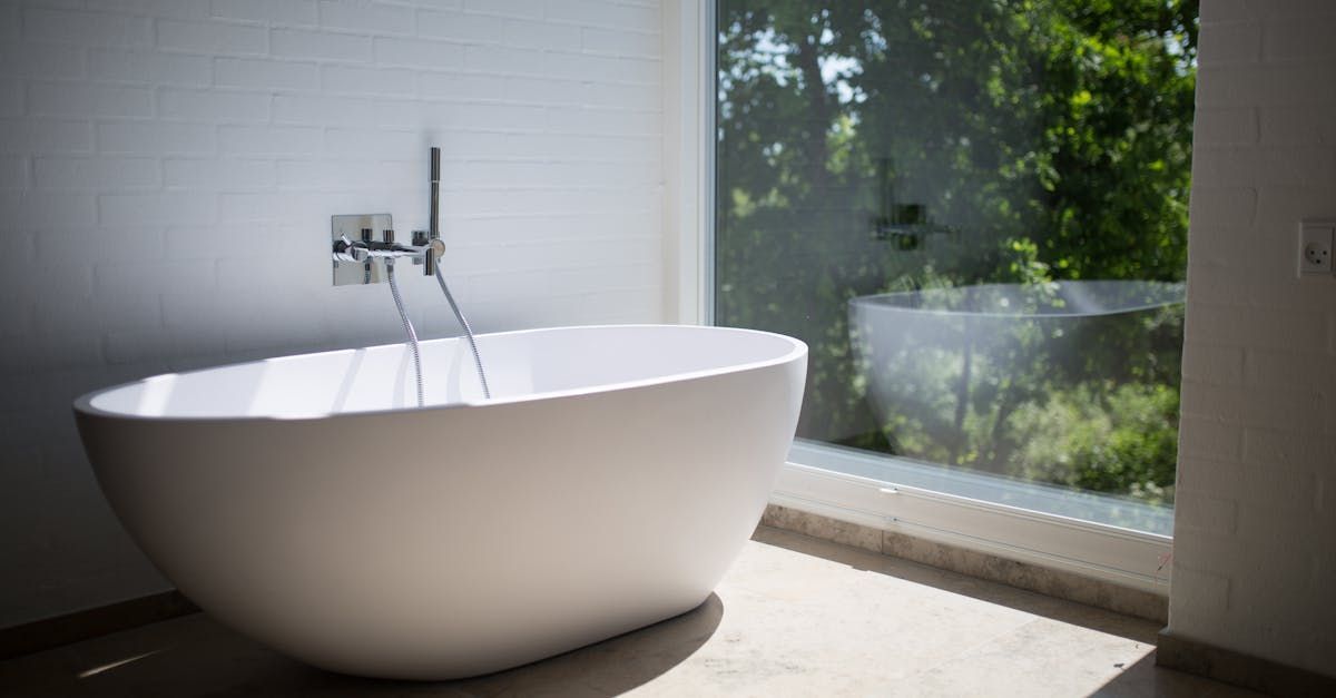 White oval bathtub next to large window overlooking greenery, in a modern bathroom.