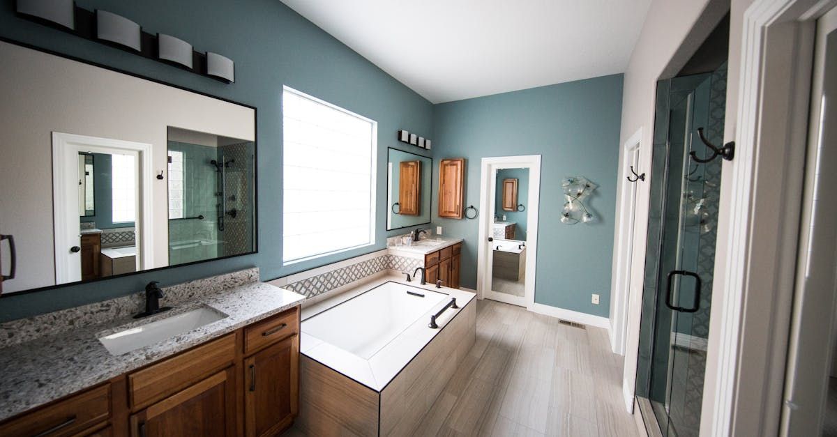 Spacious bathroom with blue walls, light wood cabinets, large mirror, soaking tub, and glass shower.