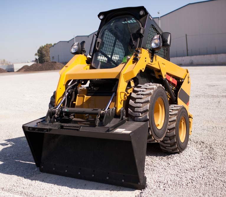 A Yellow Skid Steer With A Black Bucket Is Parked In A Gravel Lot — Austen Landscaping & Earthmoving in Deeragun, QLD
