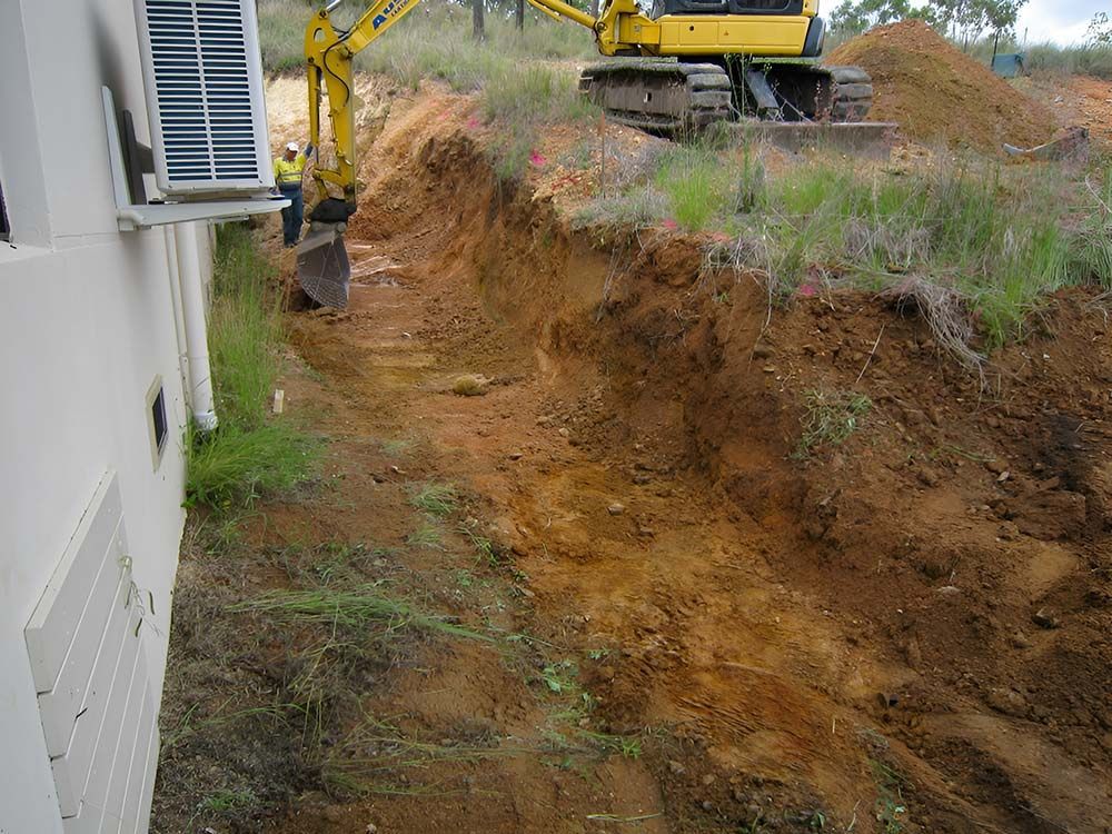 A Yellow Excavator Is Digging A Hole In The Backyard — Austen Landscaping & Earthmoving in Bushland Beach, QLD