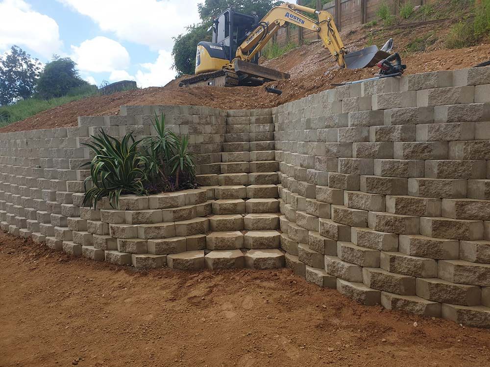 A Concrete Retaining Wall With Stairs And An Austen Excavator — Austen Landscaping & Earthmoving in Deeragun, QLD