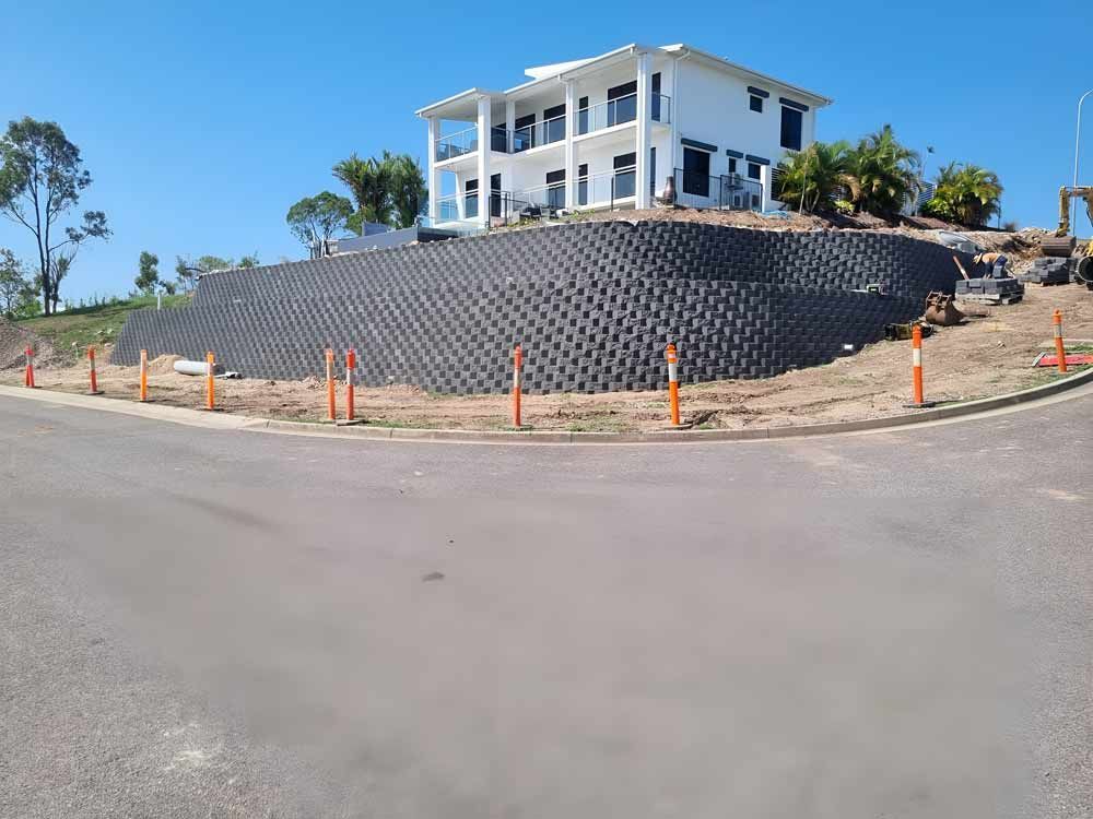 A Large White House Is Sitting On Top Of A Hill With Retaining Wall — Austen Landscaping & Earthmoving in Deeragun, QLD