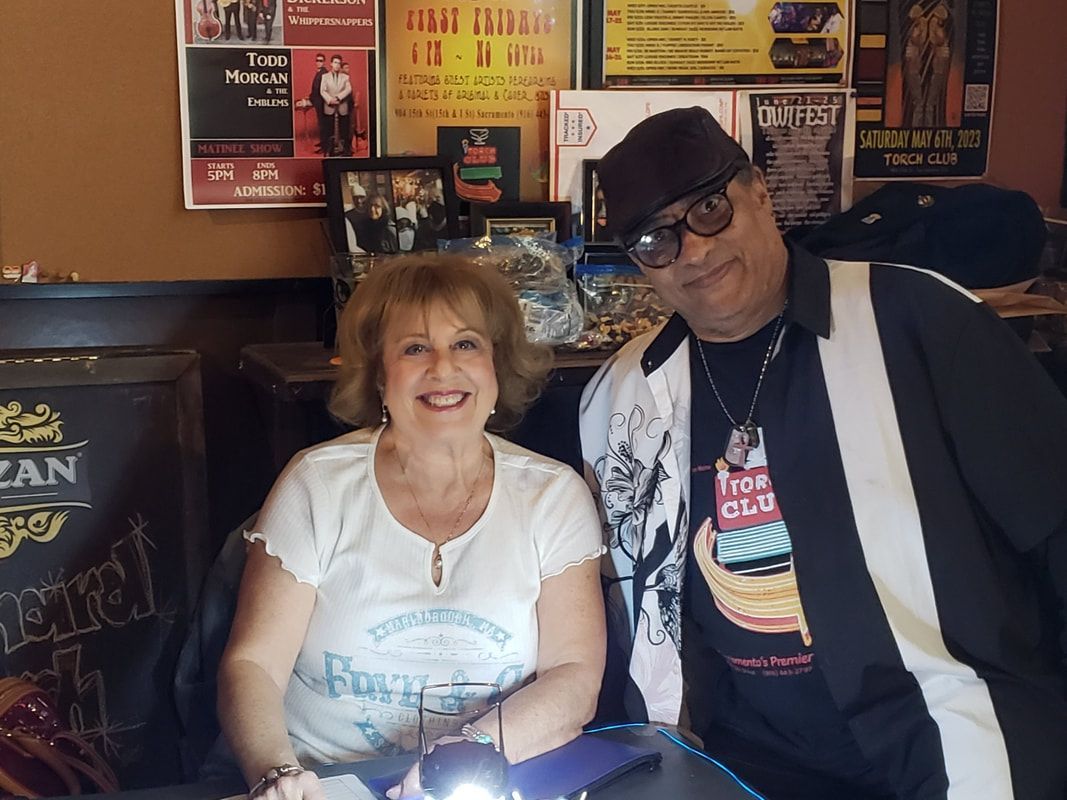 Two people smiling at a table in a cozy restaurant, with posters on the wall behind them.