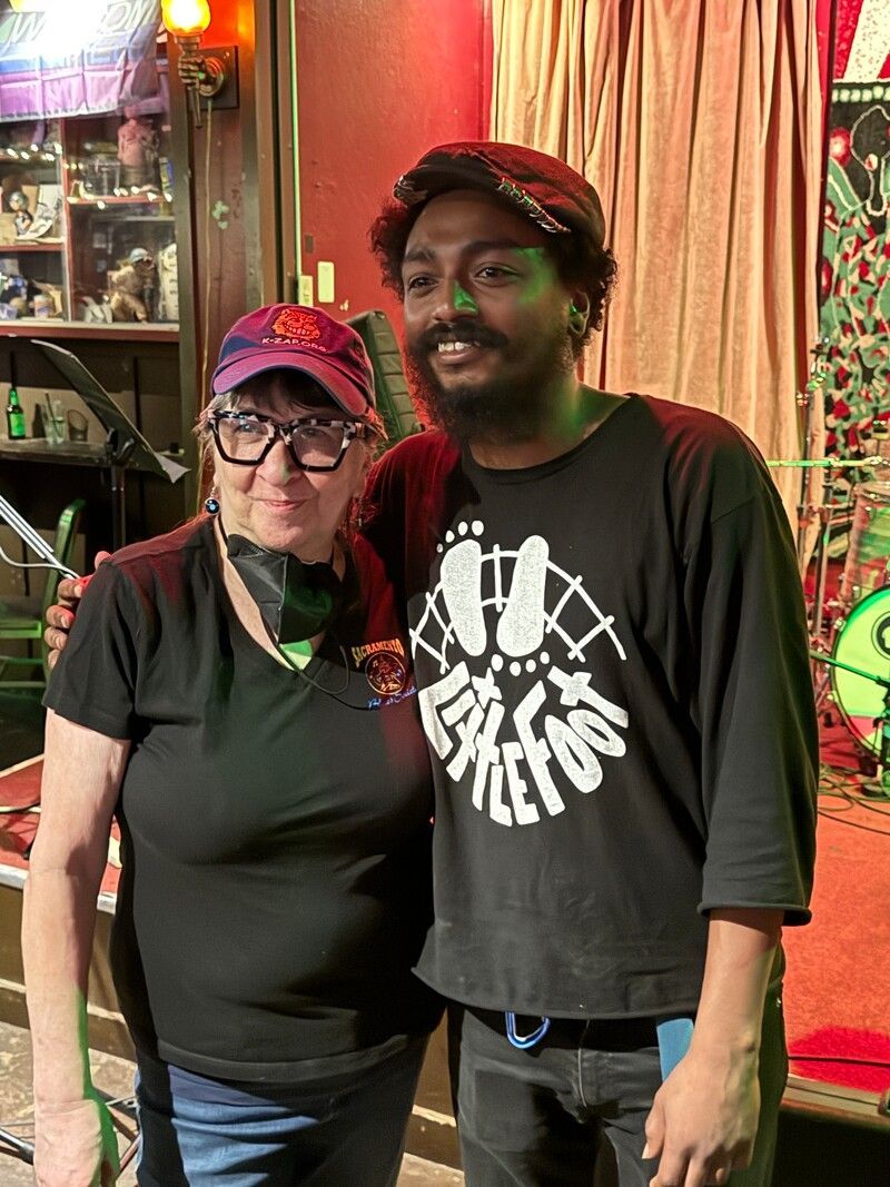 Two people standing together indoors, wearing black shirts and red hats, smiling at the camera.