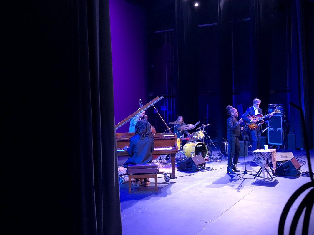 Jazz trio performing on a dimly lit stage, with a pianist, drummer, and saxophonist under purple lights