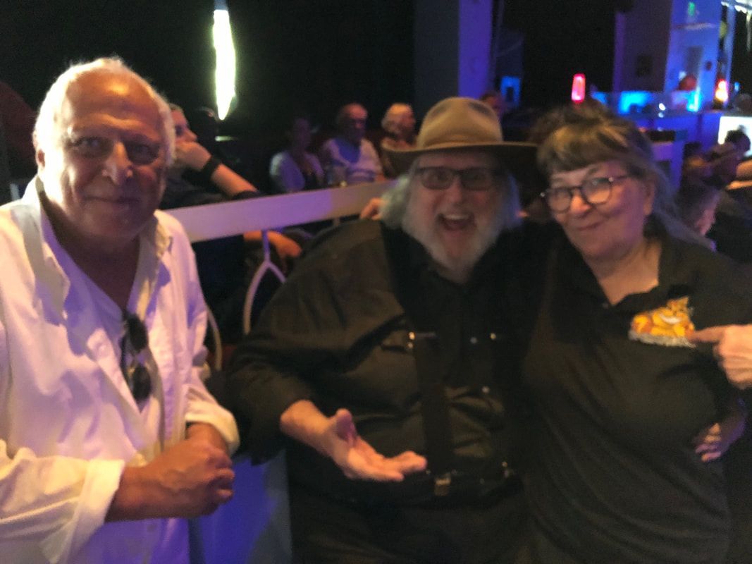 Three people posing together at a dimly lit event, smiling and standing close by a barrier.