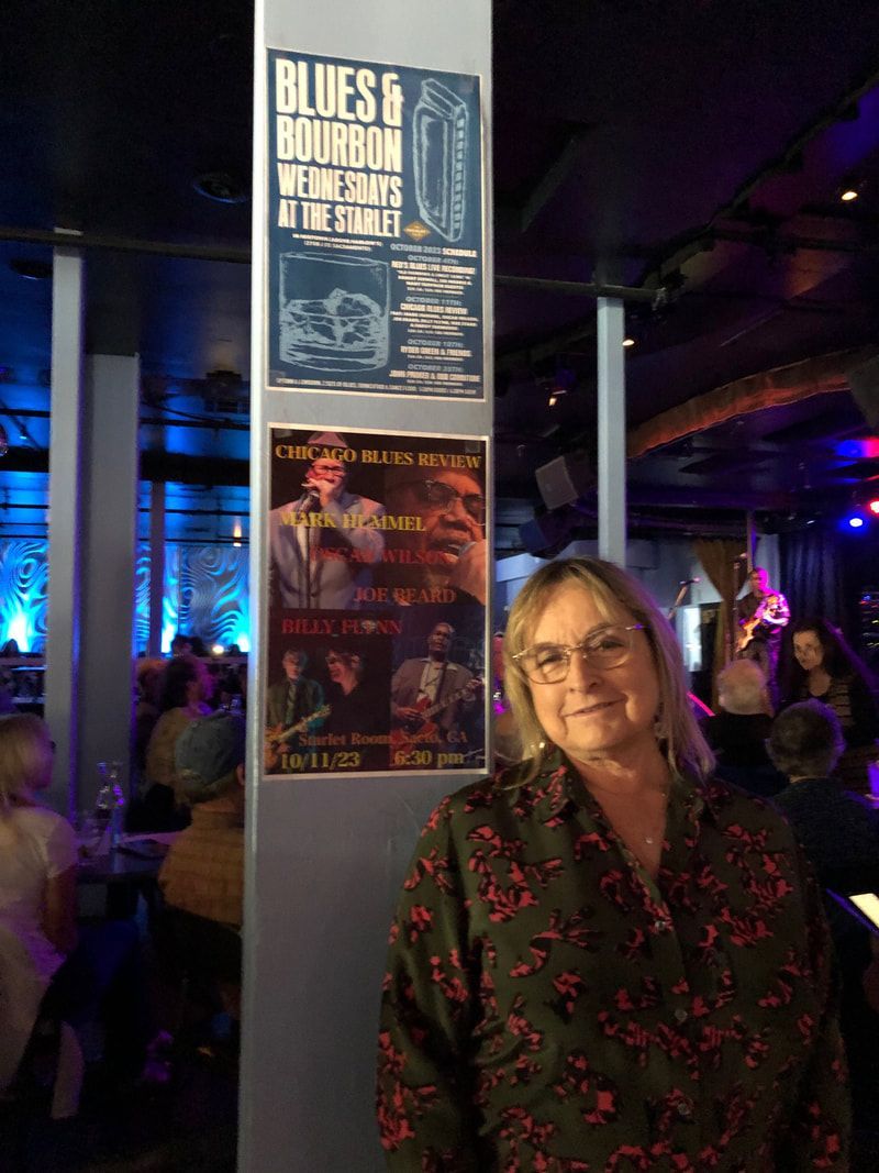 Woman standing in a dimly lit venue beside a poster-covered pillar with blue and purple lights