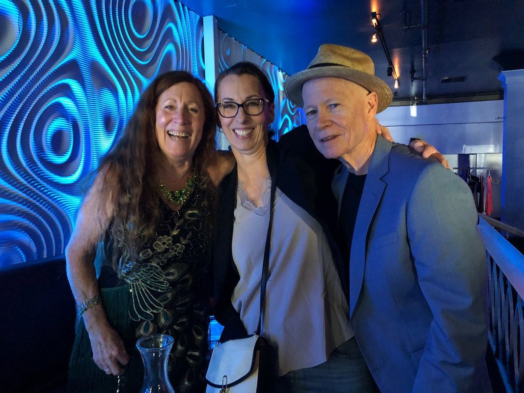 Three people smiling in a blue-lit indoor venue, standing close together.