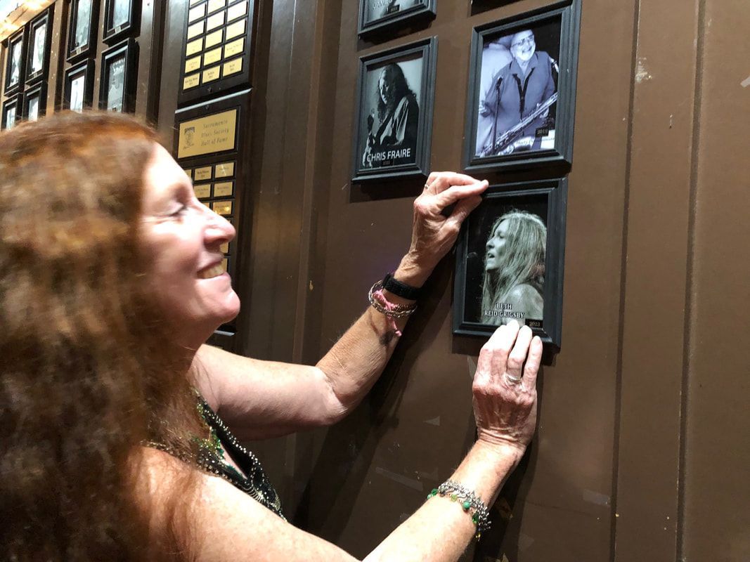 Woman touching a wall-mounted memorial with framed photos and a skull plaque