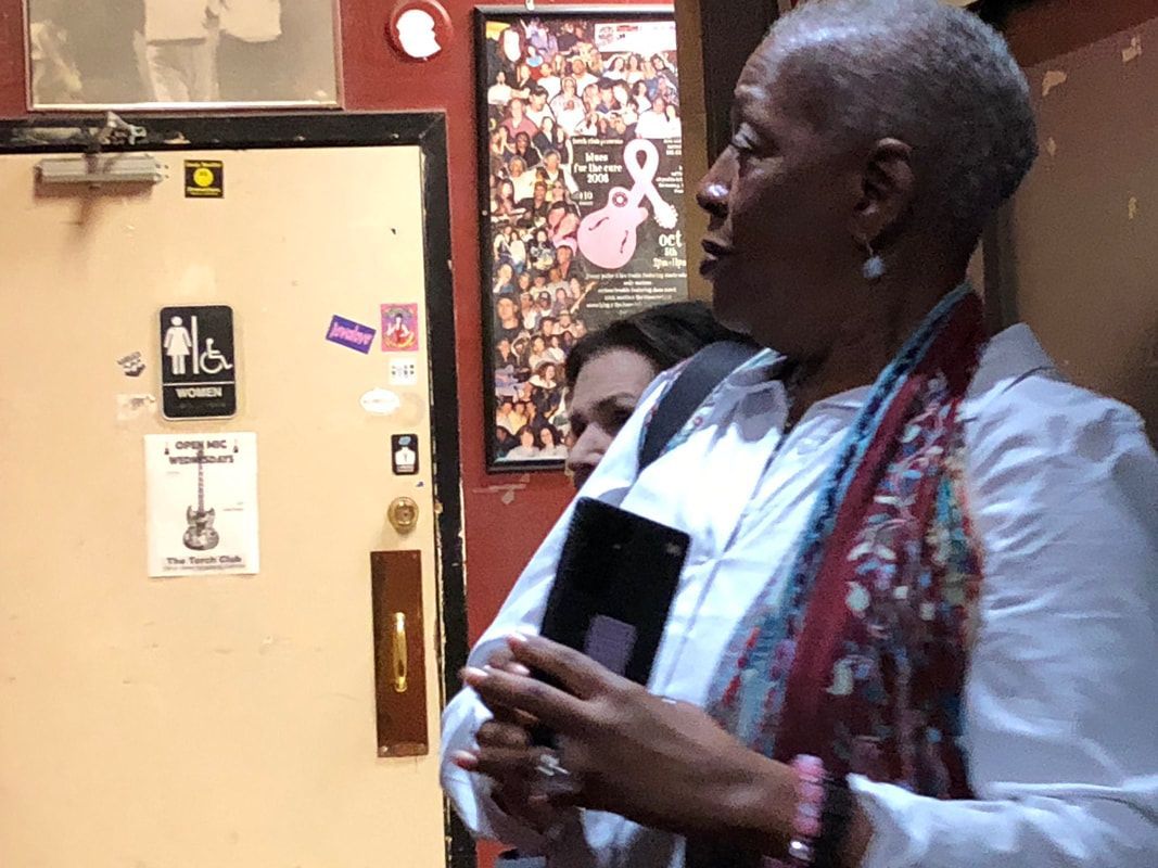 Person holding a phone stands beside a restroom door in a hallway.