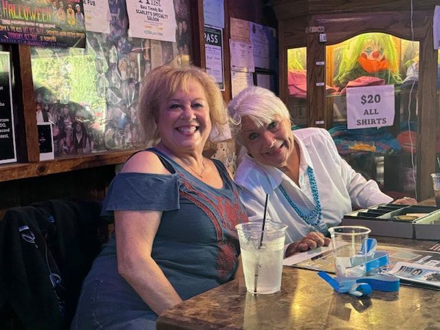 Two smiling people seated at a bar with drinks and menus in a dimly lit restaurant.