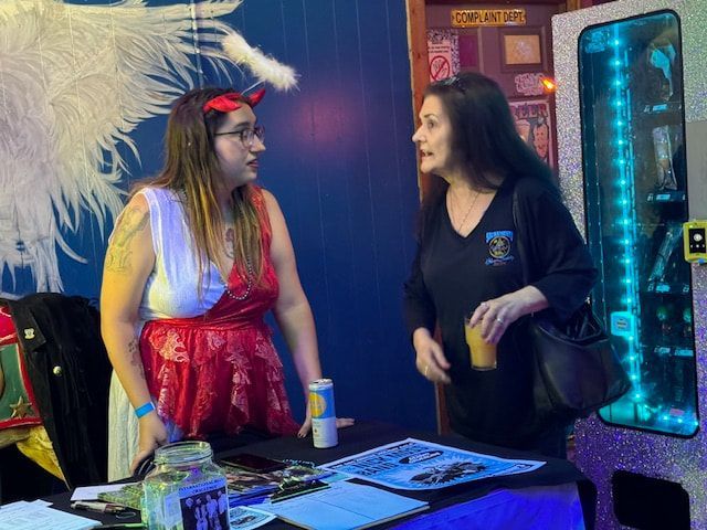 Two people talking at a convention table beside a blue-lit display case