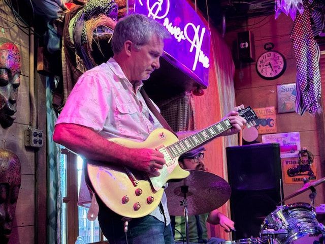 Guitarist playing a cream electric guitar on a colorful neon-lit stage