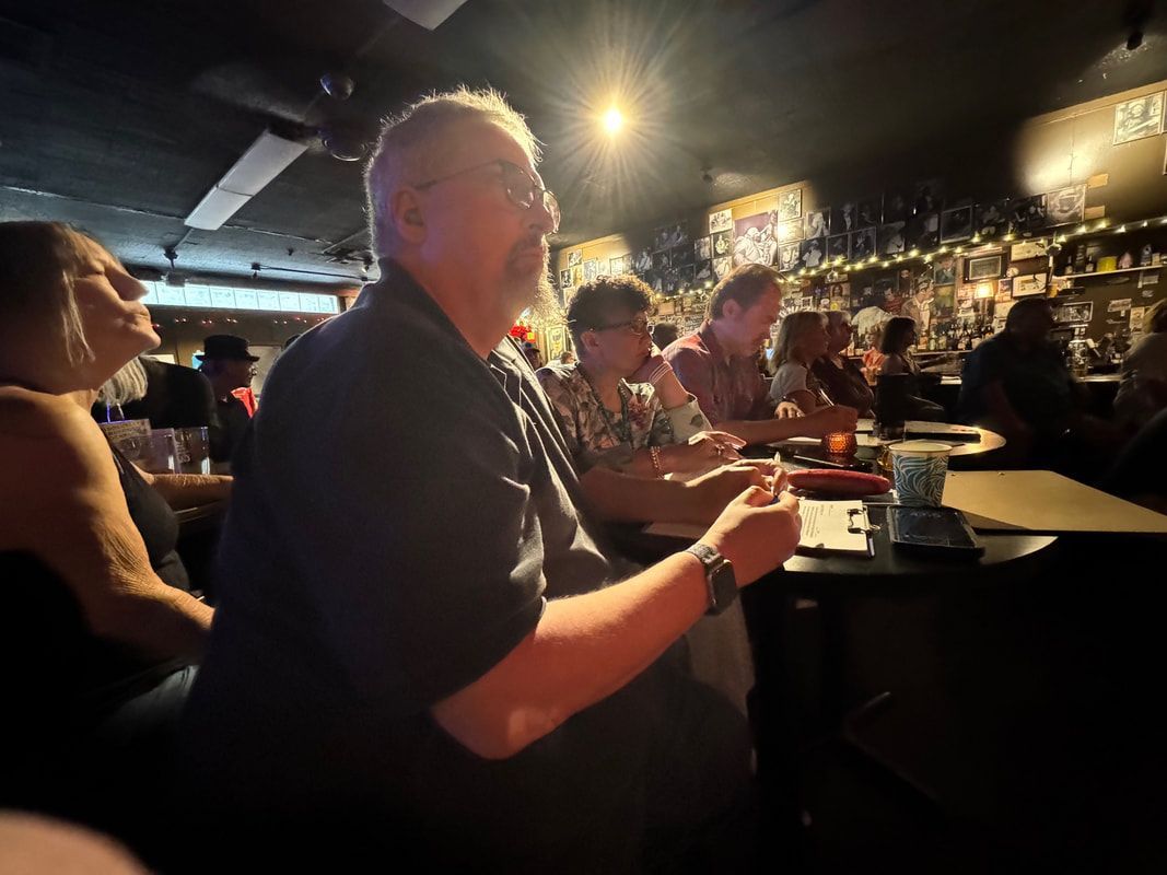 People seated at a dimly lit bar, with one person holding a drink under bright overhead lights.