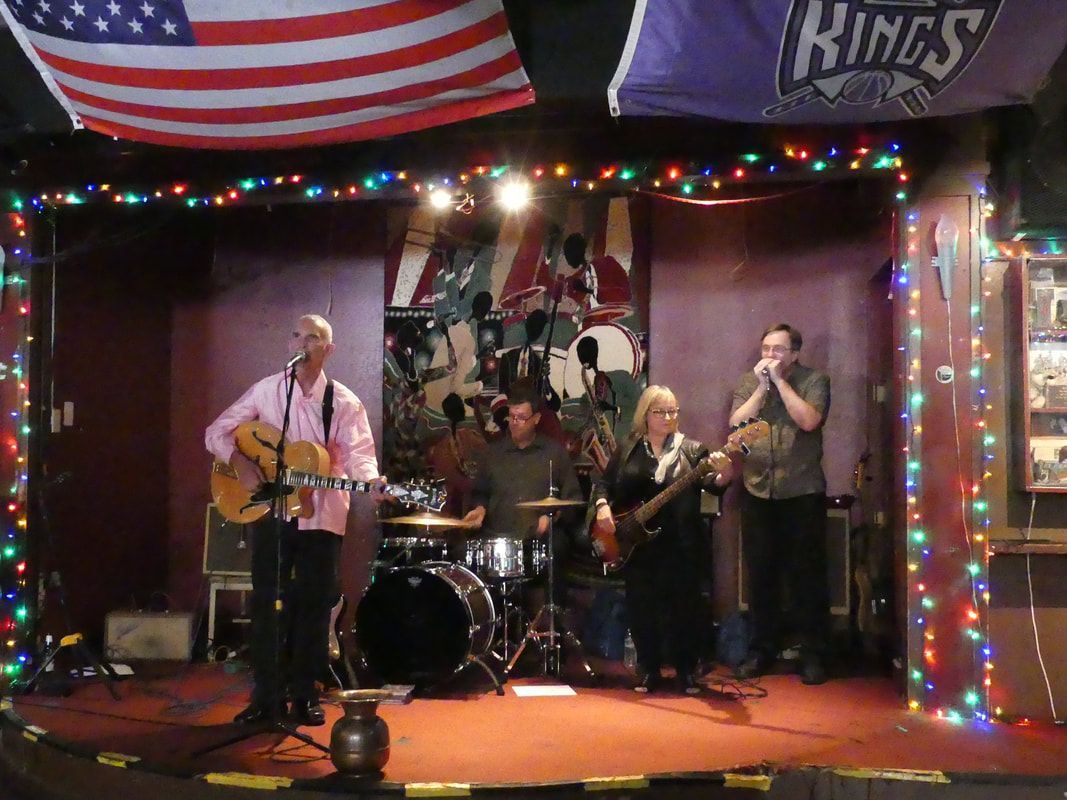 Band performing on a small stage with string lights and an American flag overhead