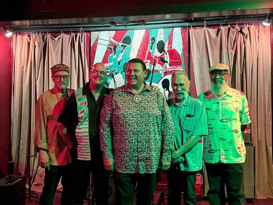 Five people standing on a small stage in front of curtains, with a colorful projected backdrop behind them.