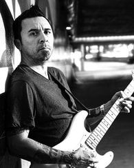 Black-and-white portrait of a person holding an electric guitar in a dimly lit indoor space