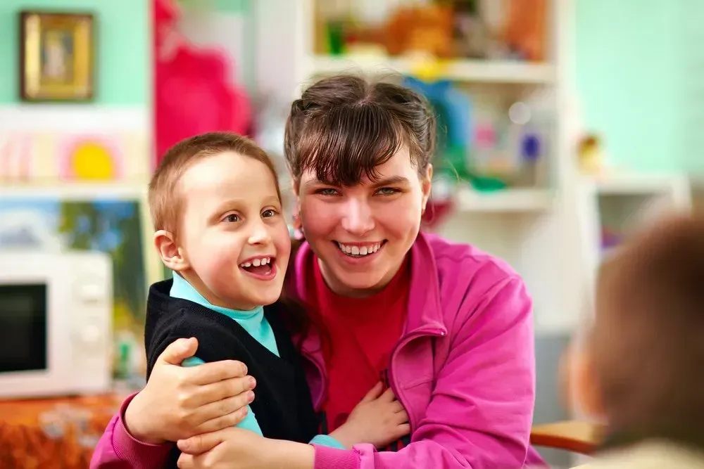 Person in a Pink Jacket Smiles While Embracing a Smiling Child — CQ Home Care in Yeppoon, QLD